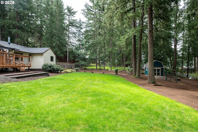 view of yard featuring fence, a storage unit, a wooden deck, and an outbuilding