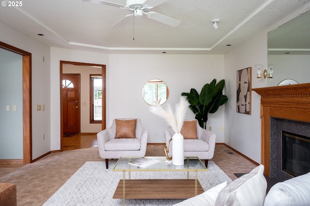 carpeted living room with ceiling fan, a glass covered fireplace, baseboards, and a raised ceiling