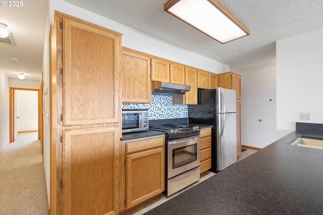 kitchen featuring stainless steel appliances, visible vents, under cabinet range hood, backsplash, and dark countertops