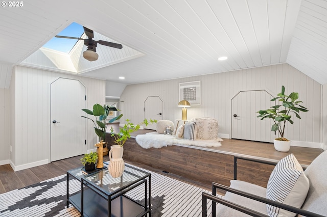 living area featuring lofted ceiling with skylight, wood finished floors, a ceiling fan, and baseboards