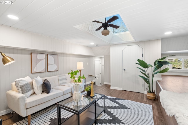 living room with a ceiling fan, vaulted ceiling with skylight, baseboards, and wood finished floors