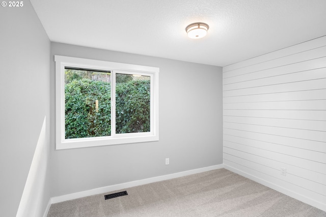 empty room featuring light carpet, a textured ceiling, visible vents, and baseboards