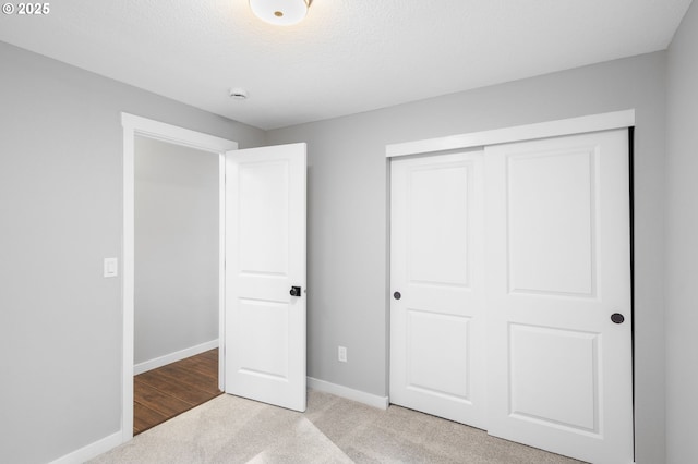 unfurnished bedroom featuring carpet floors, a closet, a textured ceiling, and baseboards