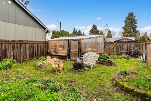 view of yard with an outdoor structure, a fenced backyard, an outdoor fire pit, and an exterior structure