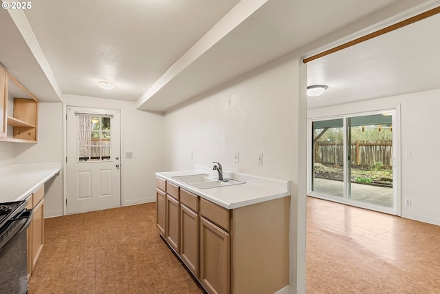 kitchen with stove, light countertops, baseboards, and a sink