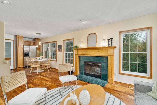 living area with visible vents, baseboards, wood finished floors, and a tiled fireplace