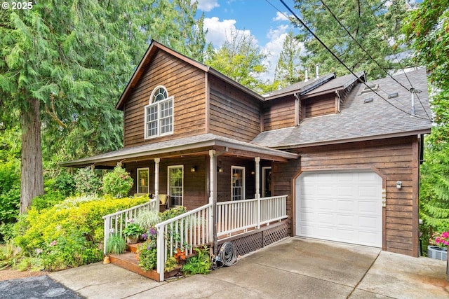 chalet / cabin featuring a shingled roof, covered porch, an attached garage, and driveway