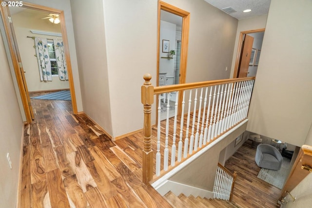 hall with baseboards, an upstairs landing, wood finished floors, and visible vents