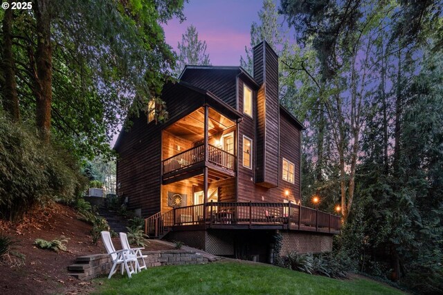 back of property at dusk featuring a lawn, a deck, a chimney, and a balcony