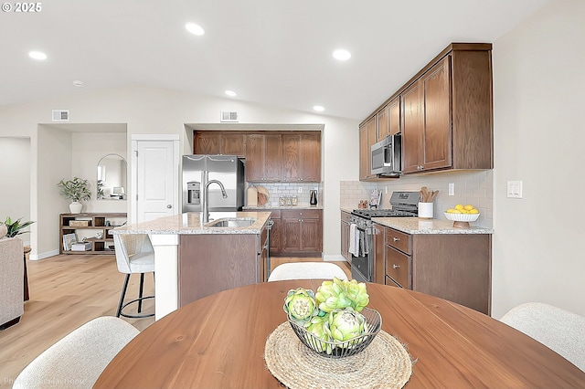 1021 Sommerville Loop, Harrisburg, OR 97446 - kitchen with stainless steel appliances, an island with sink, a sink, light wood finished floors, and tasteful backsplash
