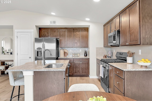 1021 Sommerville Loop, Harrisburg, OR 97446 - kitchen featuring stainless steel appliances, vaulted ceiling, a sink, light wood-style flooring, and a kitchen island with sink