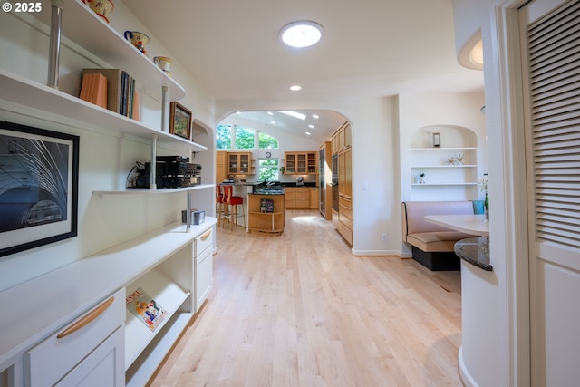 corridor featuring light wood finished floors, arched walkways, lofted ceiling, baseboards, and recessed lighting