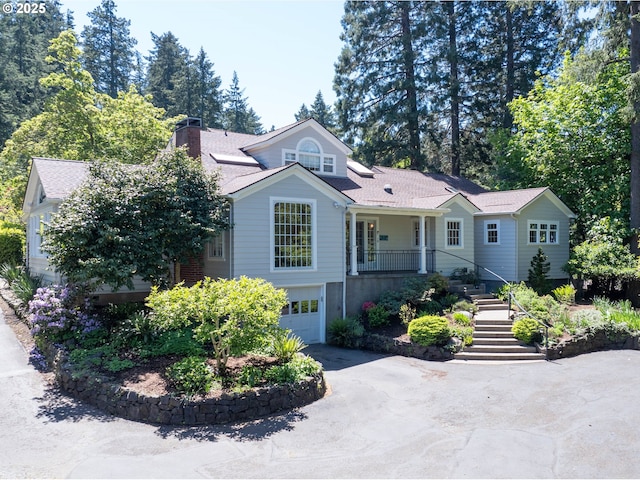 view of front of home with a garage, stairs, driveway, a chimney, and covered porch