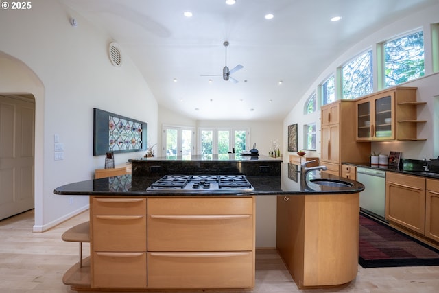 kitchen with appliances with stainless steel finishes, a sink, an island with sink, arched walkways, and dark stone counters