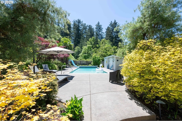 view of pool featuring a water slide, a patio area, an outbuilding, and fence