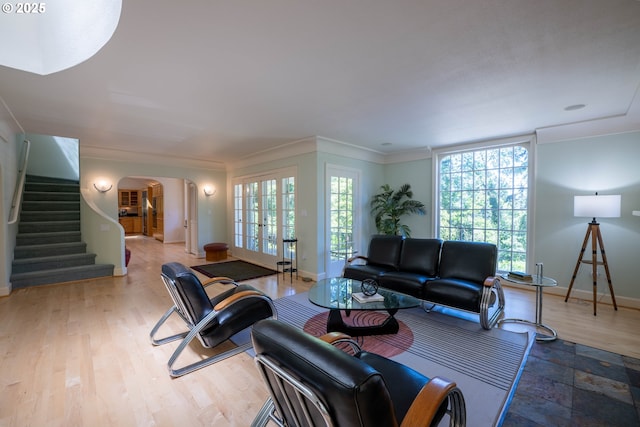 living area with arched walkways, stairway, healthy amount of natural light, baseboards, and ornamental molding