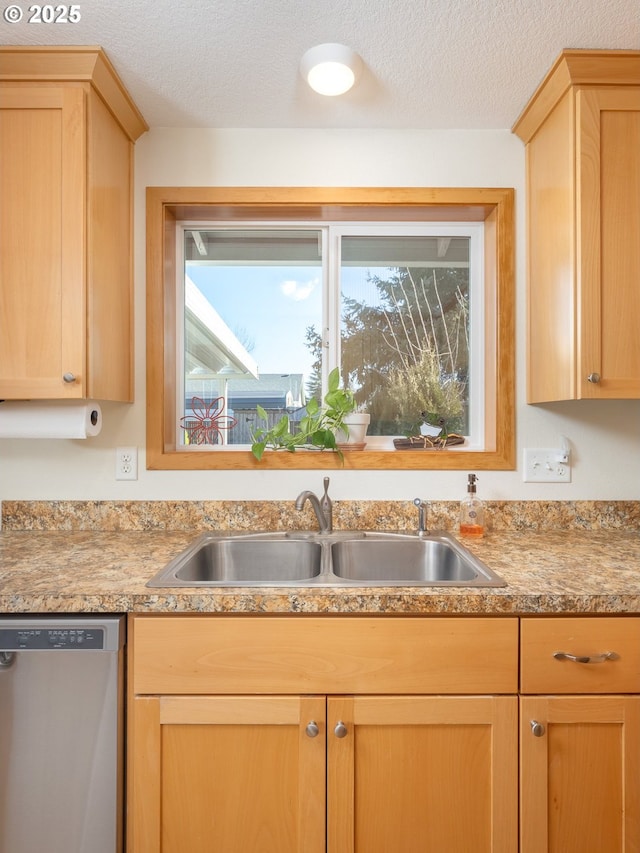 kitchen with light brown cabinetry, sink, stainless steel dishwasher, and a textured ceiling