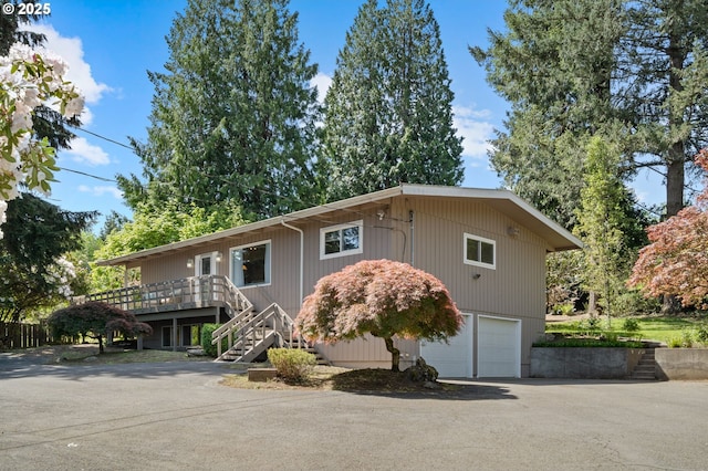 view of home's exterior featuring an attached garage, stairway, asphalt driveway, and a deck