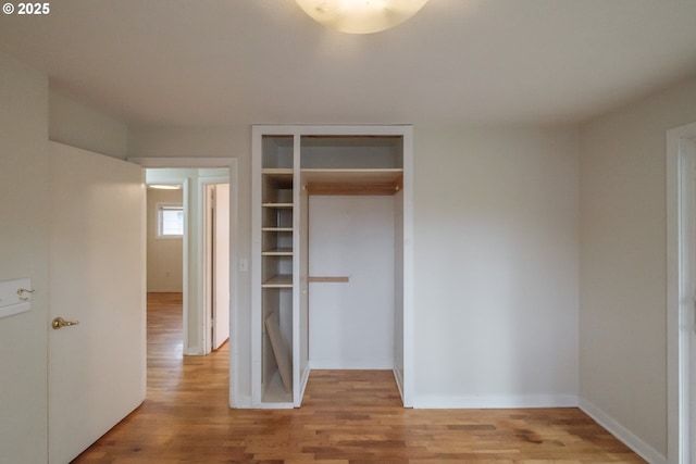 unfurnished bedroom featuring light wood finished floors, baseboards, and a closet