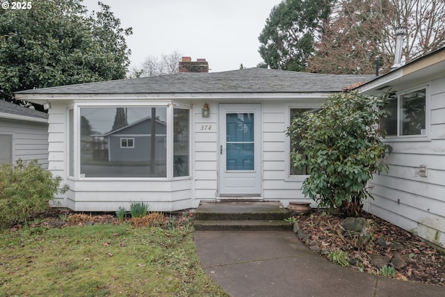 doorway to property featuring roof with shingles, a chimney, and a lawn