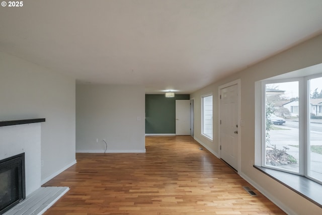 unfurnished living room with a fireplace with raised hearth, light wood-style flooring, plenty of natural light, and visible vents