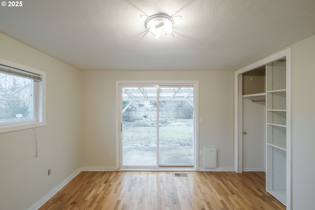 unfurnished dining area with light wood finished floors, baseboards, visible vents, and a textured ceiling