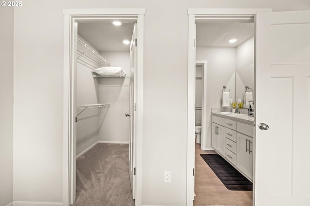 bathroom with recessed lighting, toilet, vanity, a walk in closet, and baseboards