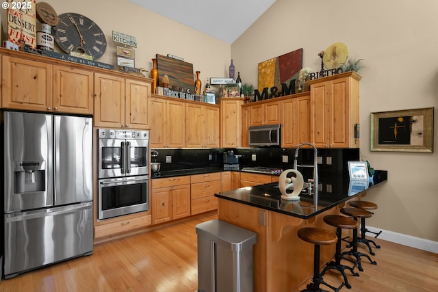 3563 Jake Mann Ln, Florence, OR 97439 - kitchen with appliances with stainless steel finishes, light wood-style flooring, decorative backsplash, a peninsula, and a breakfast bar