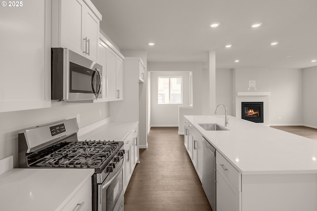 kitchen with appliances with stainless steel finishes, hardwood / wood-style floors, white cabinetry, sink, and a kitchen island with sink