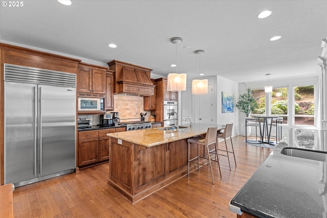 100 Garibaldi St, Lake Oswego, OR 97035 - kitchen featuring built in appliances, custom exhaust hood, brown cabinets, light wood-type flooring, and recessed lighting