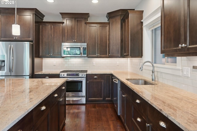 kitchen featuring stainless steel appliances, a sink, light stone counters, recessed lighting, and dark brown cabinets