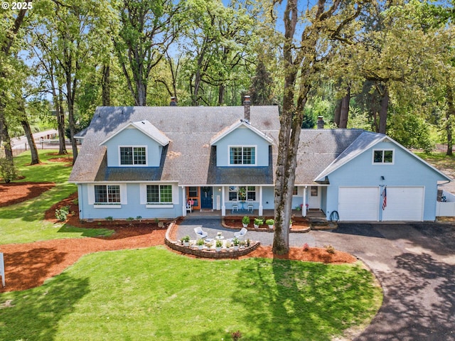 new england style home featuring covered porch, driveway, a front yard, and a garage