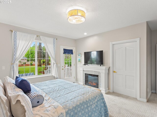 carpeted bedroom with a glass covered fireplace, baseboards, access to outside, and a textured ceiling