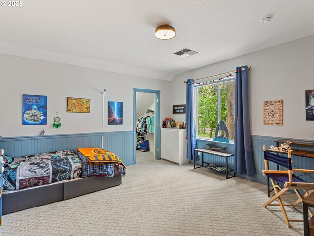 bedroom with carpet floors, visible vents, wainscoting, and a walk in closet