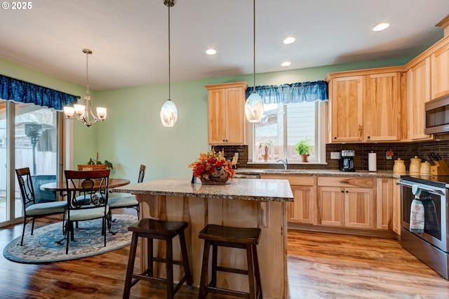 kitchen with light wood-type flooring, light brown cabinets, a center island, stainless steel appliances, and decorative backsplash