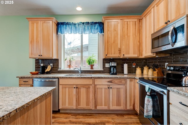 kitchen featuring light brown cabinets, light wood-style flooring, a sink, appliances with stainless steel finishes, and tasteful backsplash