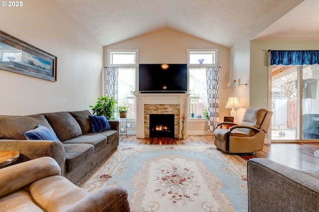 living area with a healthy amount of sunlight, wood finished floors, a fireplace, and vaulted ceiling