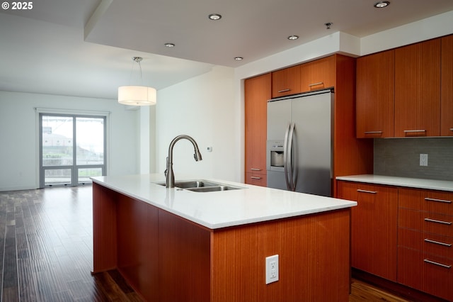 kitchen with decorative light fixtures, a center island with sink, stainless steel refrigerator with ice dispenser, decorative backsplash, and sink