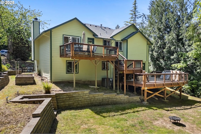 back of property with a fire pit, stairway, a wooden deck, a chimney, and a lawn
