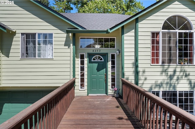 doorway to property featuring a garage, roof with shingles, and a wooden deck