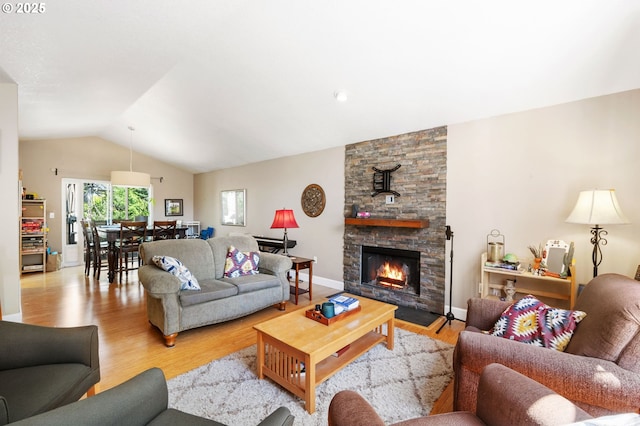 living area with baseboards, vaulted ceiling, a stone fireplace, and wood finished floors
