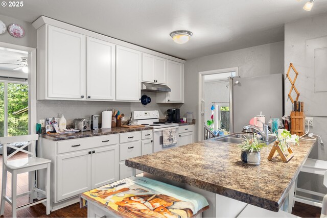 1495 N Hemlock St, Coquille, OR 97423 - kitchen with electric range, a kitchen breakfast bar, under cabinet range hood, white cabinetry, and ceiling fan