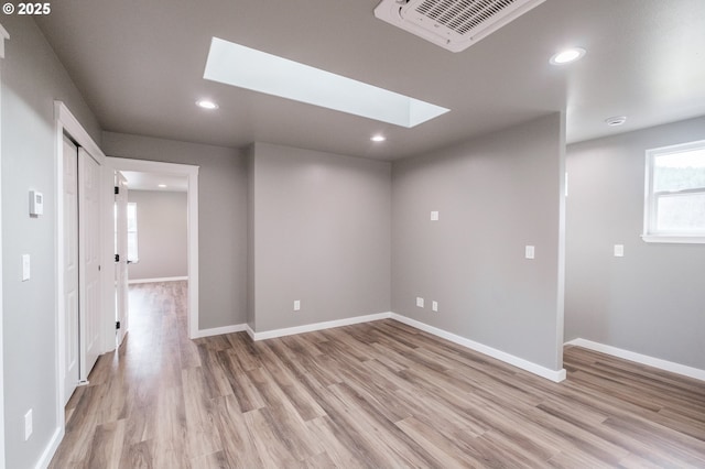 empty room featuring a skylight and light hardwood / wood-style floors