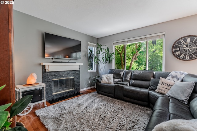 living area featuring wood finished floors, a stone fireplace, and baseboards