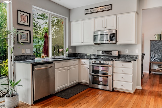 kitchen featuring appliances with stainless steel finishes, a sink, white cabinets, and light wood-style floors