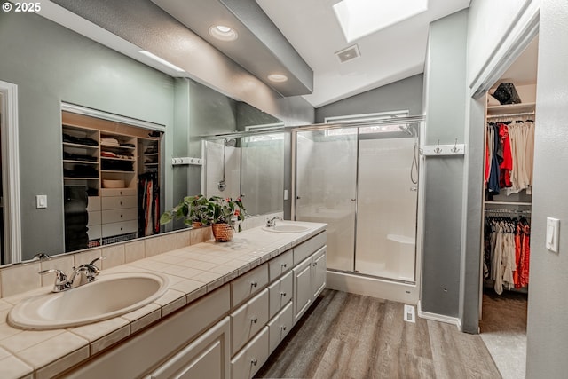 full bath with wood finished floors, a shower stall, vaulted ceiling, double vanity, and recessed lighting