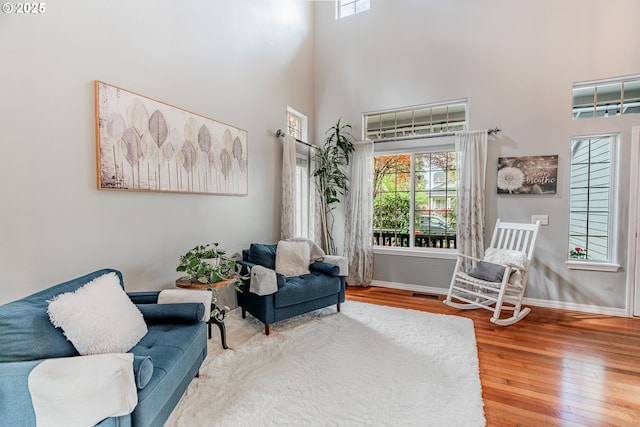 living area featuring plenty of natural light, baseboards, wood finished floors, and a high ceiling