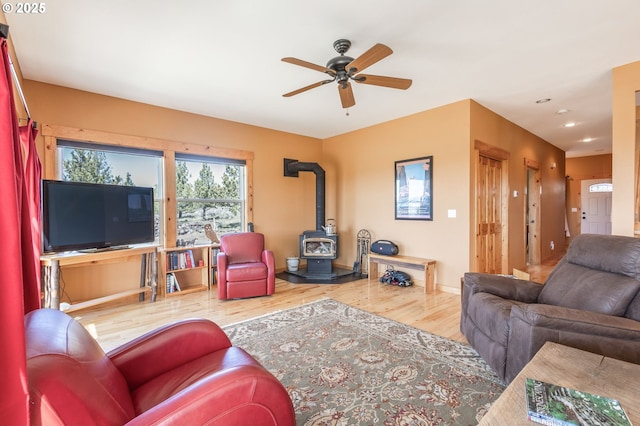 living area featuring a wood stove, recessed lighting, ceiling fan, baseboards, and wood finished floors