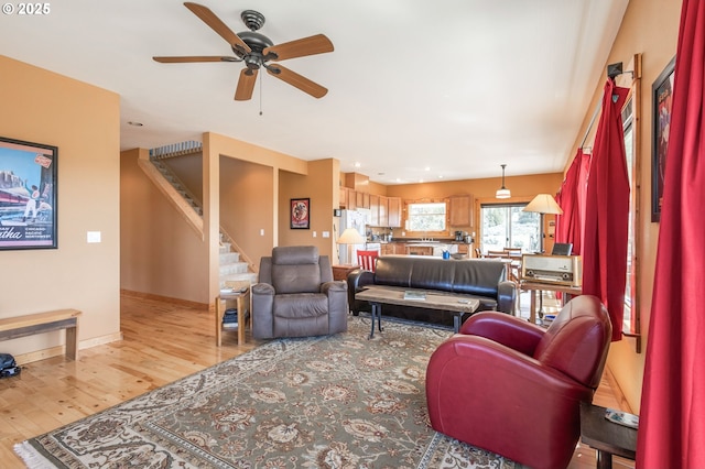 living room featuring light wood-type flooring, stairway, a ceiling fan, and baseboards