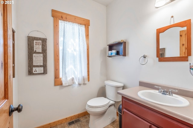 half bathroom with baseboards, visible vents, toilet, and vanity